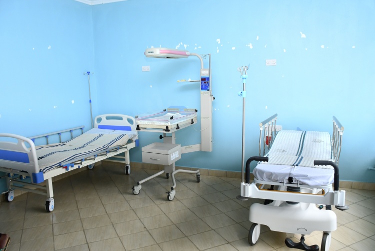 A delivery room with mother's bed and a modern bed with a heater for the baby